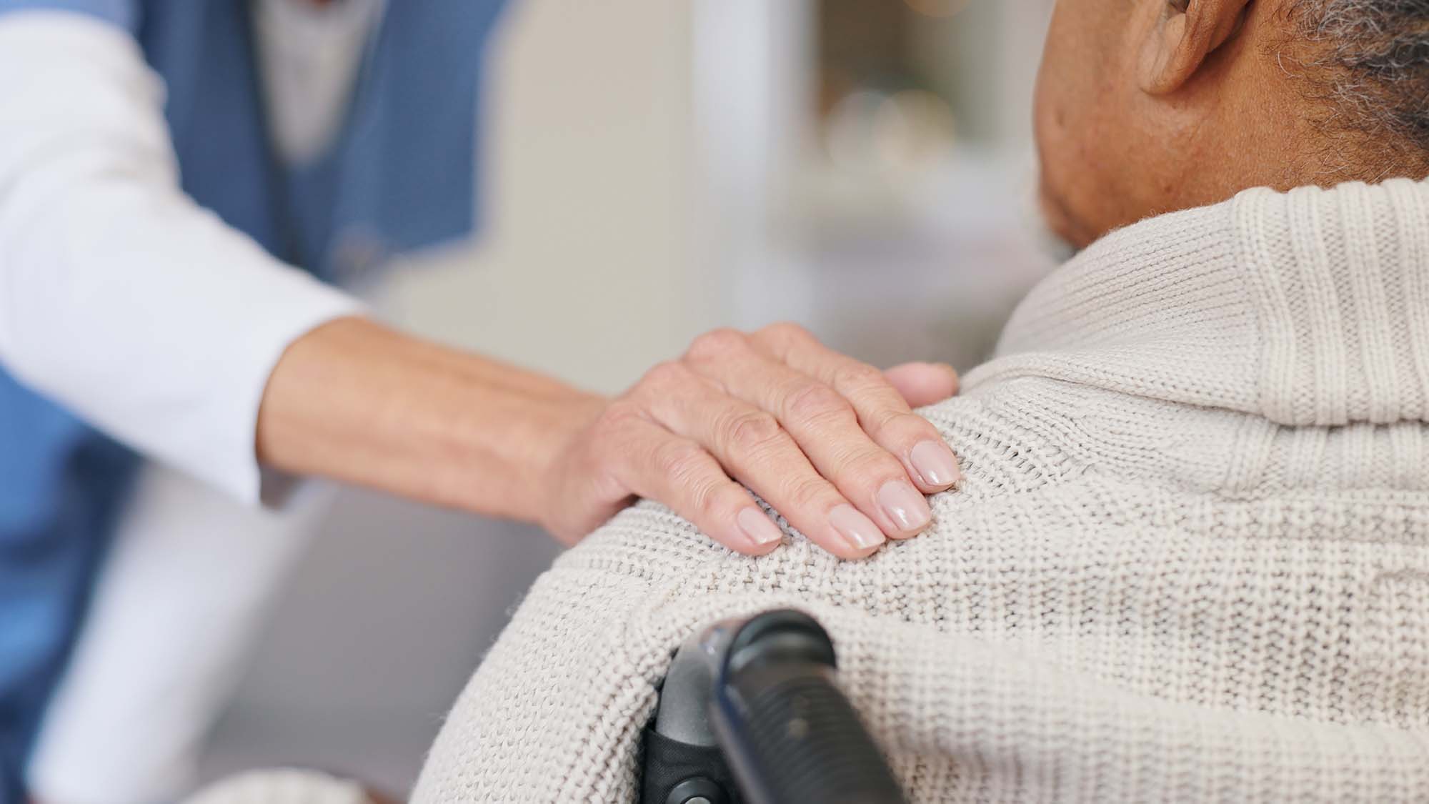 An older woman in a wheelchair listening to a doctor with someone standing behind her with their hands on her shoulders